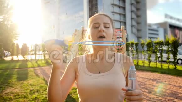 日落时分公园里美丽微笑的年轻女子吹肥皂泡的特写慢镜头视频的预览图