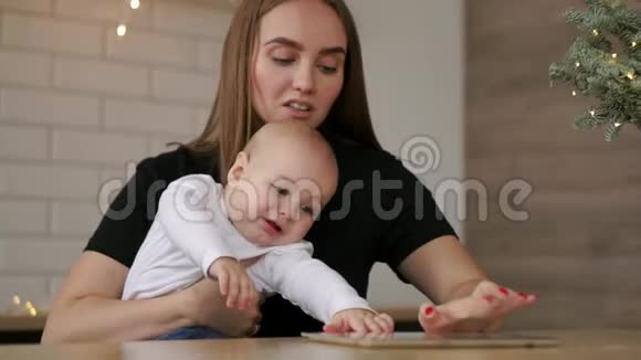 妈妈和宝宝坐在桌子旁玩平板电脑手指按在屏幕上笑着视频的预览图