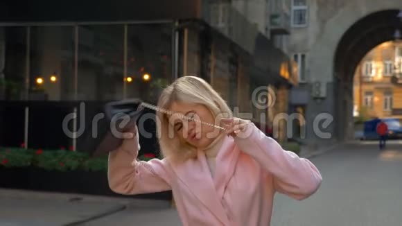 一个年轻漂亮的金发女郎穿着粉红色的外套站在现代建筑的背景下视频的预览图