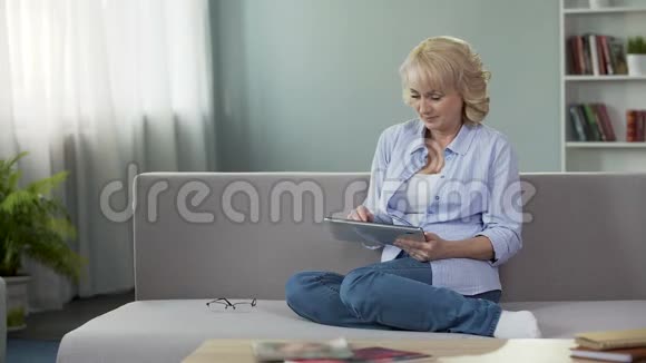 美丽的成熟女人坐在沙发上在网上购物看着镜头视频的预览图