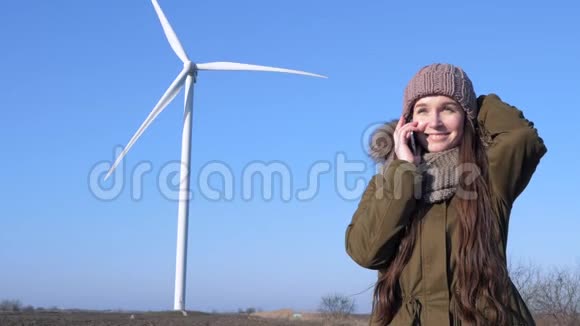 干净的力量手里拿着手机的女孩微笑着在现代风车和天空的背景下用电话交谈视频的预览图