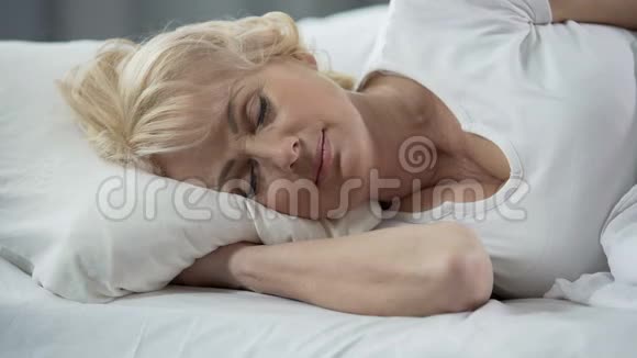 一位美丽的金发成熟女士躺在床上健康的睡眠退休视频的预览图