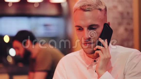年轻的帅哥在夜间咖啡馆的智能手机上聊天他坐在霓虹灯招牌旁边喝着鸡尾酒视频的预览图