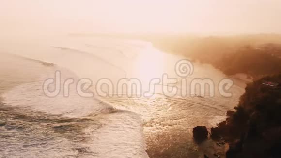 海洋和波浪在温暖的日落或日出带岩石海岸的空中景色视频的预览图