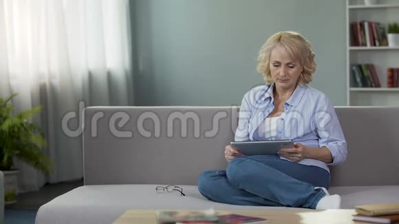 成年妇女坐在沙发上拿着平板电脑在网上买新眼镜视频的预览图