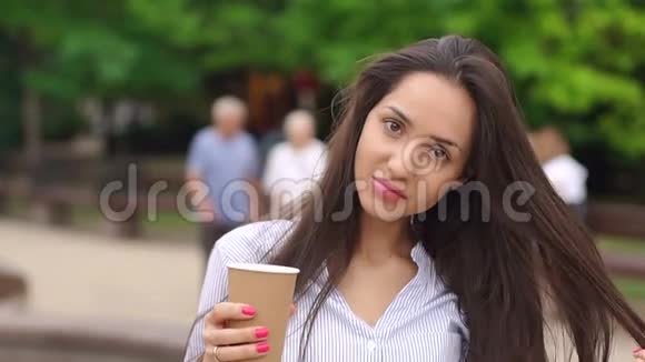 一个女孩在拥挤的公园里喝咖啡的肖像视频的预览图
