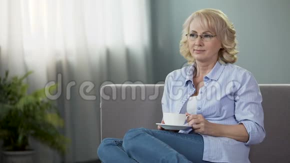 快乐的老年妇女坐在沙发上喝茶健康和退休视频的预览图