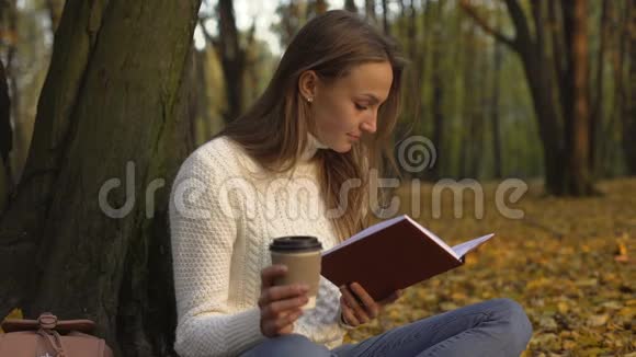 女学生在温暖的秋日坐在美丽的公园里看书视频的预览图