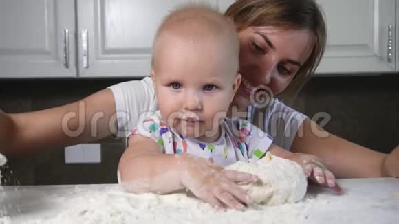 年轻的母亲和她的孩子准备面团把面粉倒在桌子上小宝宝玩面粉家庭视频的预览图