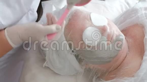 美容院的理疗程序戴着白手套的美容师在厚厚的脸上涂抹海藻酸钠面膜视频的预览图