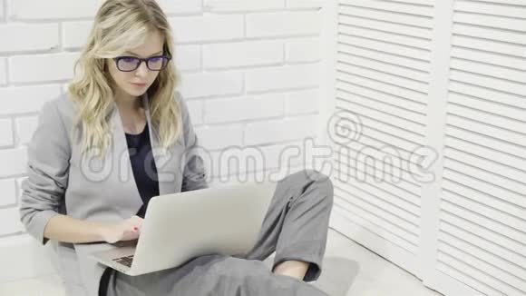 戴着眼镜在地板上的笔记本电脑上打字的漂亮女商人视频的预览图