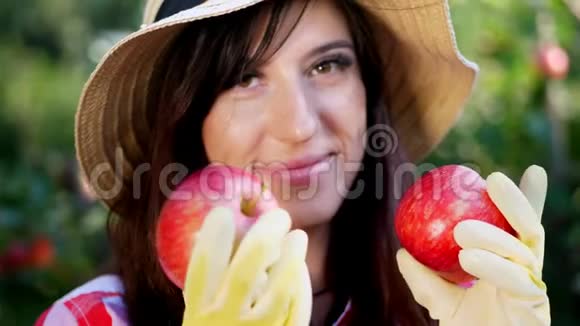 特写肖像一个女农民戴着帽子和手套手里拿着两个大红苹果摘苹果视频的预览图