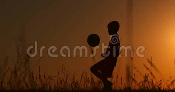 剪影一个男孩在日落时在田里戏耍一个球视频的预览图