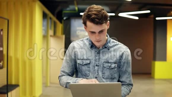 一个有魅力的年轻帅哥手里拿着笔记本电脑走在某个地方室内镜头慢动作视频的预览图