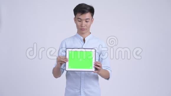 年轻快乐的亚洲商人一边思考一边展示数码平板电脑视频的预览图