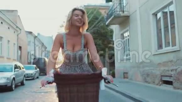 迷人的金发美女穿着时髦的裙子骑着老式的自行车骑着一辆明亮的自行车沿着荒凉的城市街道行驶视频的预览图