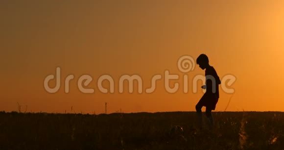 日落时一个男孩踢足球的剪影日落时一个男孩在田里玩杂耍视频的预览图
