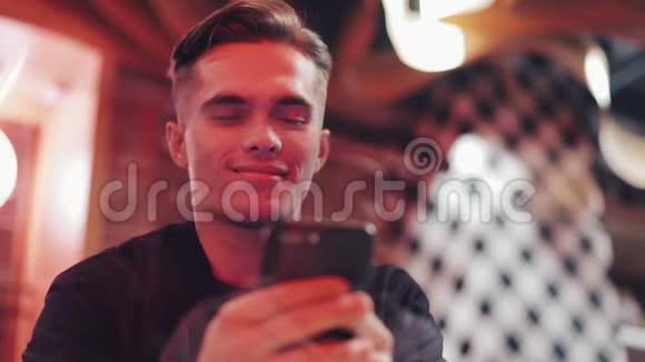 年轻有魅力的男人晚上用智能手机他坐在靠近霓虹灯标志的酒吧或餐馆里关门视频的预览图