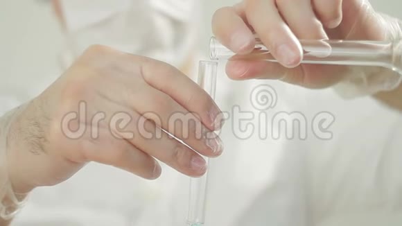 一名身穿白衣的男医生和防护手套将蓝色液体倒入试管中视频的预览图