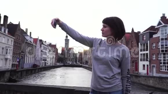 女孩游客在比利时布鲁日日落时在智能手机上自拍慢动作视频的预览图