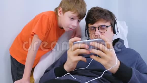 戴着眼镜和耳机的男人和他的儿子在智能手机里玩游戏玩家放松视频的预览图