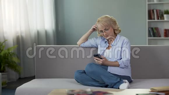 相当年长的女性坐在沙发上用智能手机计算预算视频的预览图