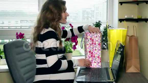 孕妇看着网上买的婴儿衣服彩色包和笔记本电脑视频的预览图