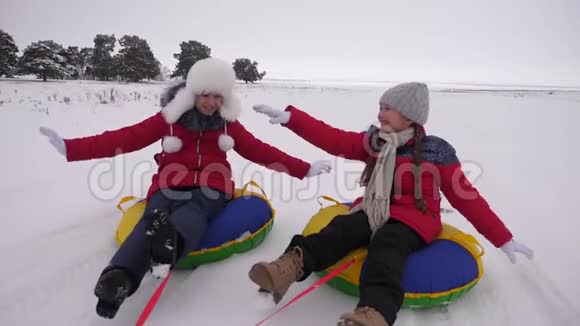快乐的孩子们在冬天的雪地里雪橇挥舞着他们的手孩子们在雪地上滑在管子上欢笑和欢乐视频的预览图