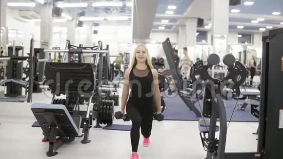 年轻迷人的女性健美运动员用手中的哑铃表演蹲健身和锻炼保健视频的预览图