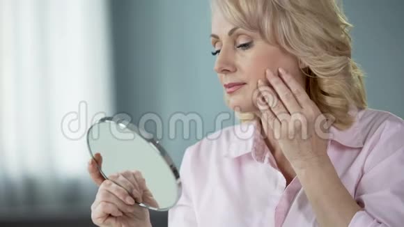 50多岁的女士照镜子对皮肤的提升感到欣喜视频的预览图