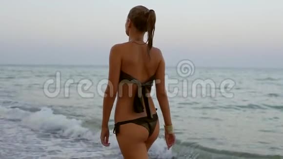 傍晚在海滩边水边散步的湿马尾辫女人的后景慢镜头视频的预览图