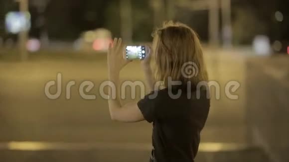 美丽的年轻女子在夜街拍智能手机视频的预览图