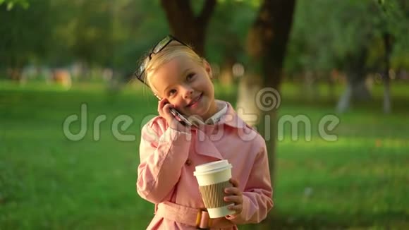 可爱的粉红色小女孩微笑着在公园里打电话视频的预览图