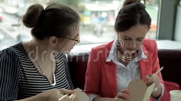 午餐时两个年轻的商务女孩坐在盒子里吃美味的面条喝咖啡工作午餐视频的预览图