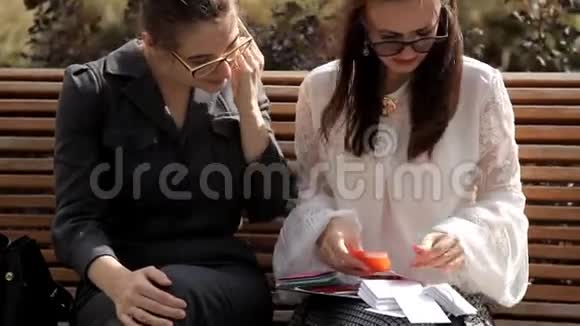 夏天两个年轻的商务女孩坐在商务中心附近的公园里考虑彩色卡片视频的预览图