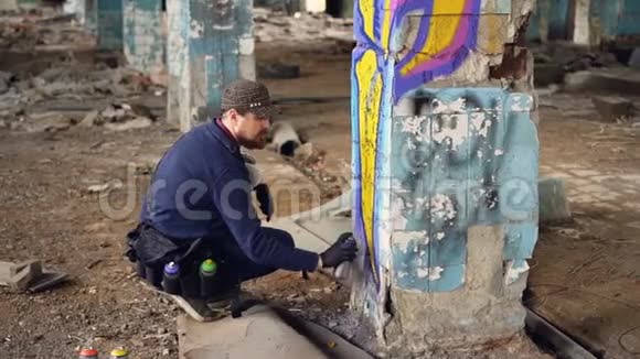 涂鸦艺术家留着胡子的家伙正在废弃建筑的柱子上用气溶胶喷漆画空工业视频的预览图