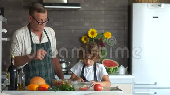 一个男孩切黄瓜做沙拉成熟的人赞美他现代厨房祖父教他孙子做饭视频的预览图