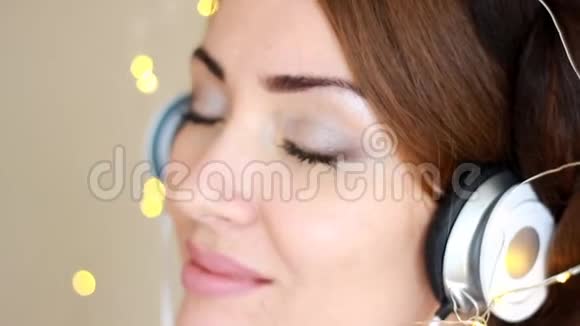 一位戴着耳机听着音乐歌曲的美女的特写肖像眼睛闭着灯视频的预览图