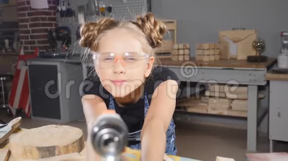 一幅有趣的10岁女孩的画像她穿着木工拿着一台电子钻对着镜头摆姿势小建筑视频的预览图