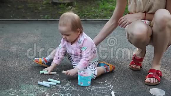 可爱的小女孩和她的母亲在夏天公园的人行道上用粉笔画画家庭母亲和人的概念视频的预览图