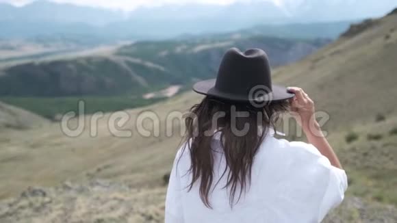 漂亮的黑发女人戴着帽子和白色衬衫在山里享受着大自然穿着衬衫的漂亮年轻女子视频的预览图