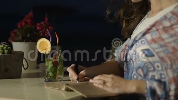 夜间在户外餐厅用记事本写诗歌的灵感女人的手视频的预览图