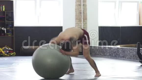 运动青年在健身球上滚动练习平衡视频的预览图
