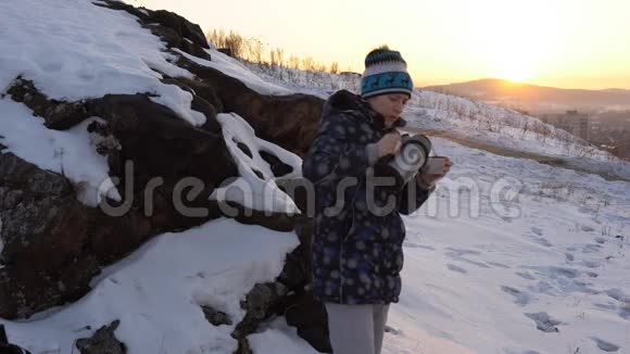 一个年轻的女人在城市附近的山上喝热水瓶里的茶或咖啡视频的预览图