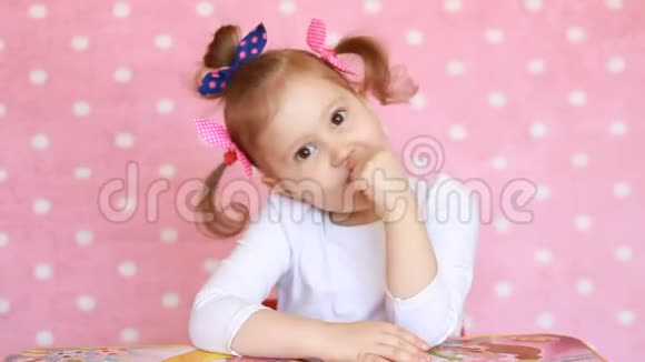 可爱有趣的宝贝女孩看着相机微笑粉色背景特写中可爱宝宝的肖像视频的预览图