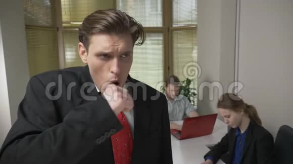 穿西装的年轻人咳嗽生病是一种疾病的概念男人和背景的女孩在办公室工作视频的预览图
