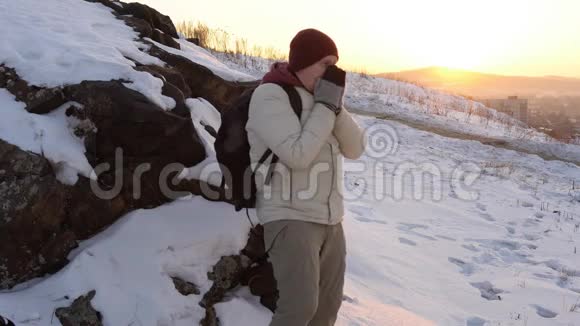 一个年轻人在冬天日落时用呼吸温暖他冻僵的手视频的预览图
