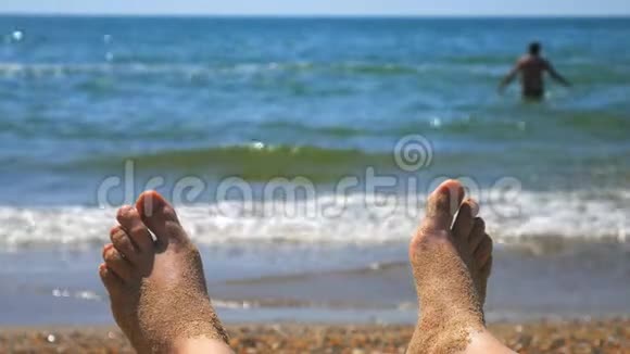 女性的双脚在沙滩上晒日光浴沙滩上有海浪女性的双脚裸露在沙滩上视频的预览图