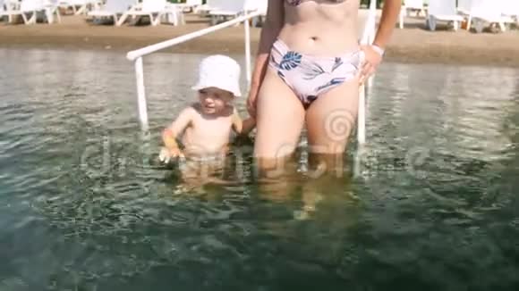 4k视频年轻母亲手抱刚学步的儿子在沙滩上的海水中散步视频的预览图