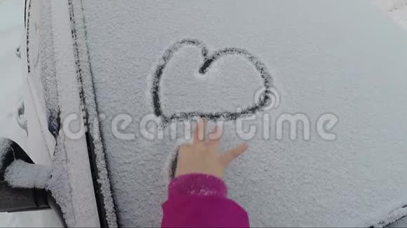 在冬天孩子的手在覆盖着雪的汽车玻璃上画了许多心视频的预览图